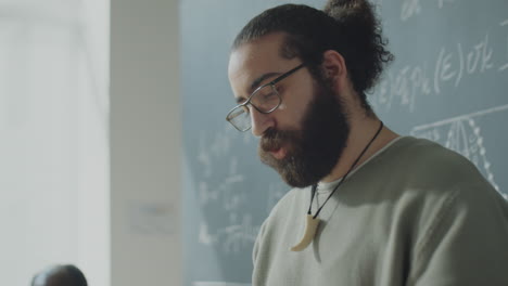 a bearded man with glasses in front of a chalkboard filled with mathematical equations