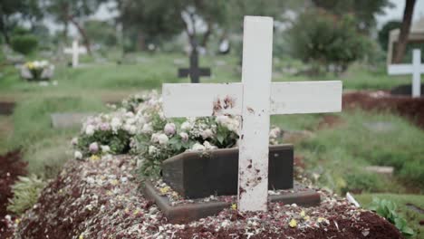 tumba cristiana con cruz blanca y ramos de flores en el cementerio visto desde atrás