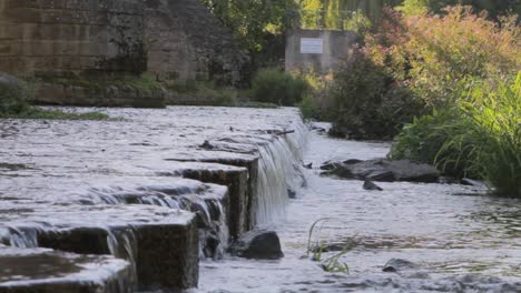 Tranquila-Cascada-Del-Río-En-Un-Entorno-Exuberante,-La-Luz-Del-Sol-Filtrándose-A-Través-Del-Follaje