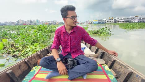 Young-Male-freelance-creator-travelling-on-wooden-boat-in-Bangladesh