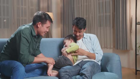 happy asian gay fathers and their cute son relaxing on couch at home