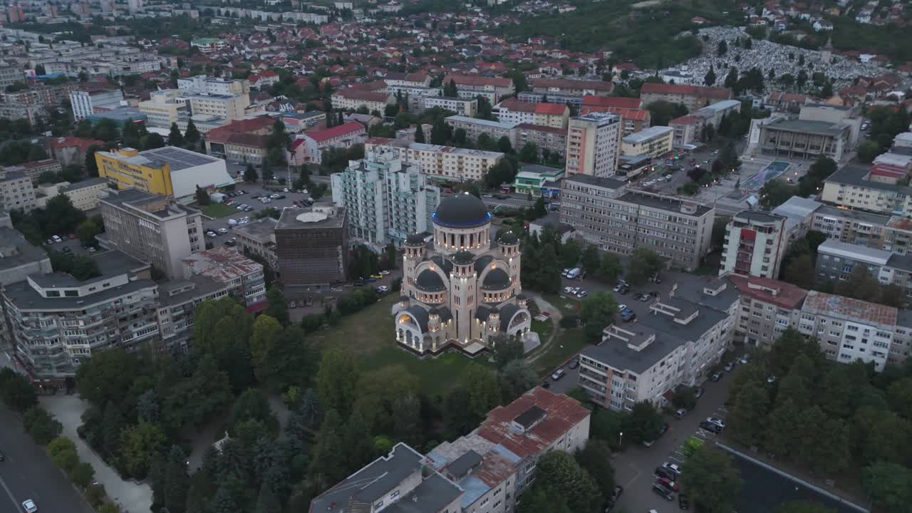 A stunning nighttime aerial view of Catedrala Adormirea Maicii Domnului in Deva, beautifully illuminated against the dark city
