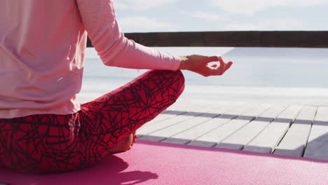 Midsection-of-mixed-race-woman-practicing-yoga-outdoors,-sitting-meditating-by-the-sea