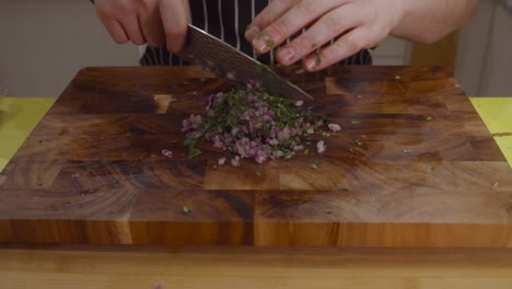 chef chops onion and herbs on a cutting board