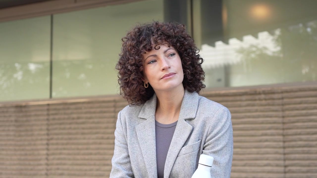 Una donna allegra con i capelli ricci tiene felicemente una bottiglia d'acqua all'aperto, immersa nella natura.
