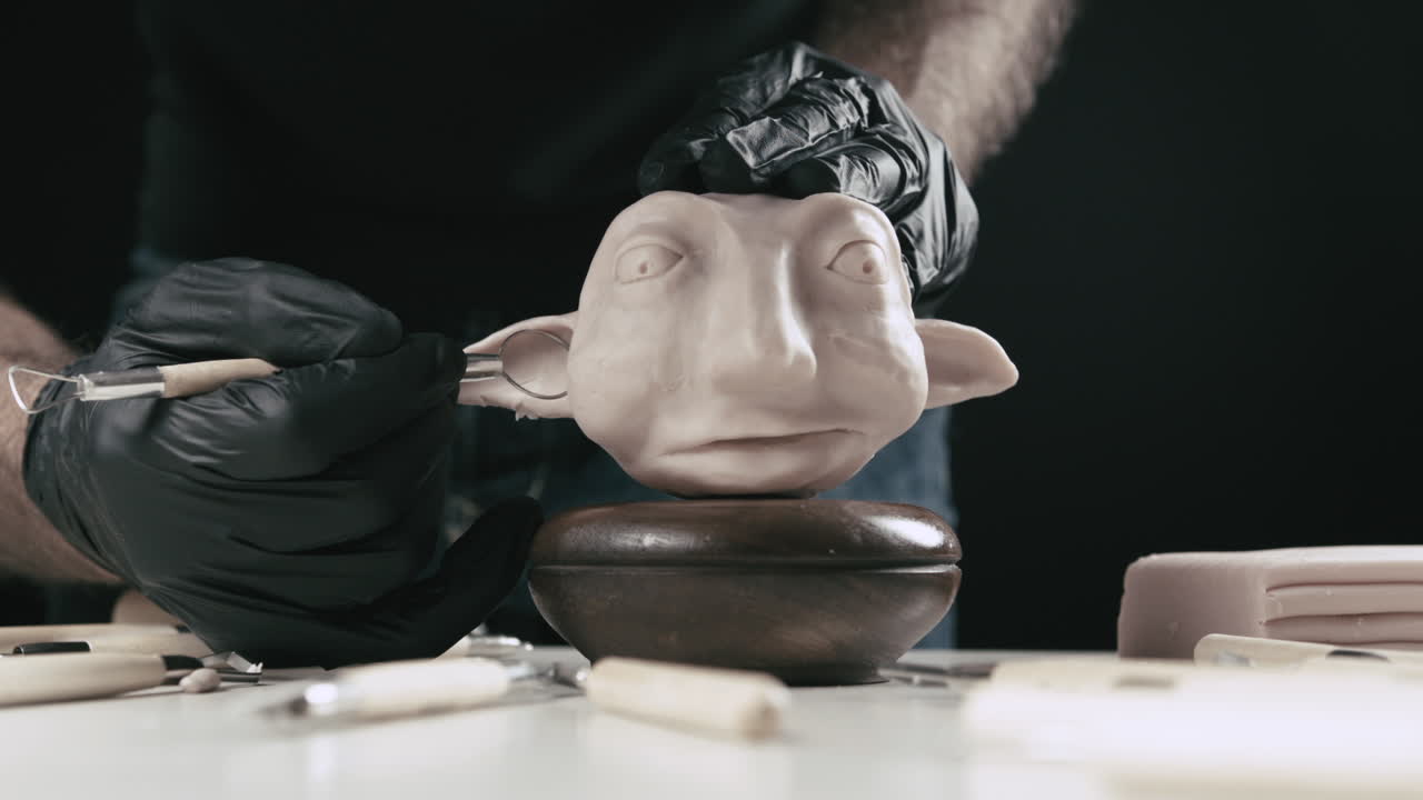 아티스트는 리본 도구로 플라스틱 인형 머리의 귀를 모델링합니다.