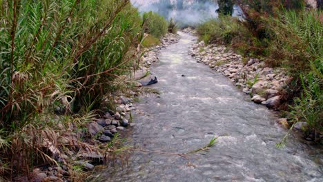 pathway of water flowing in river sided with stones and green grass