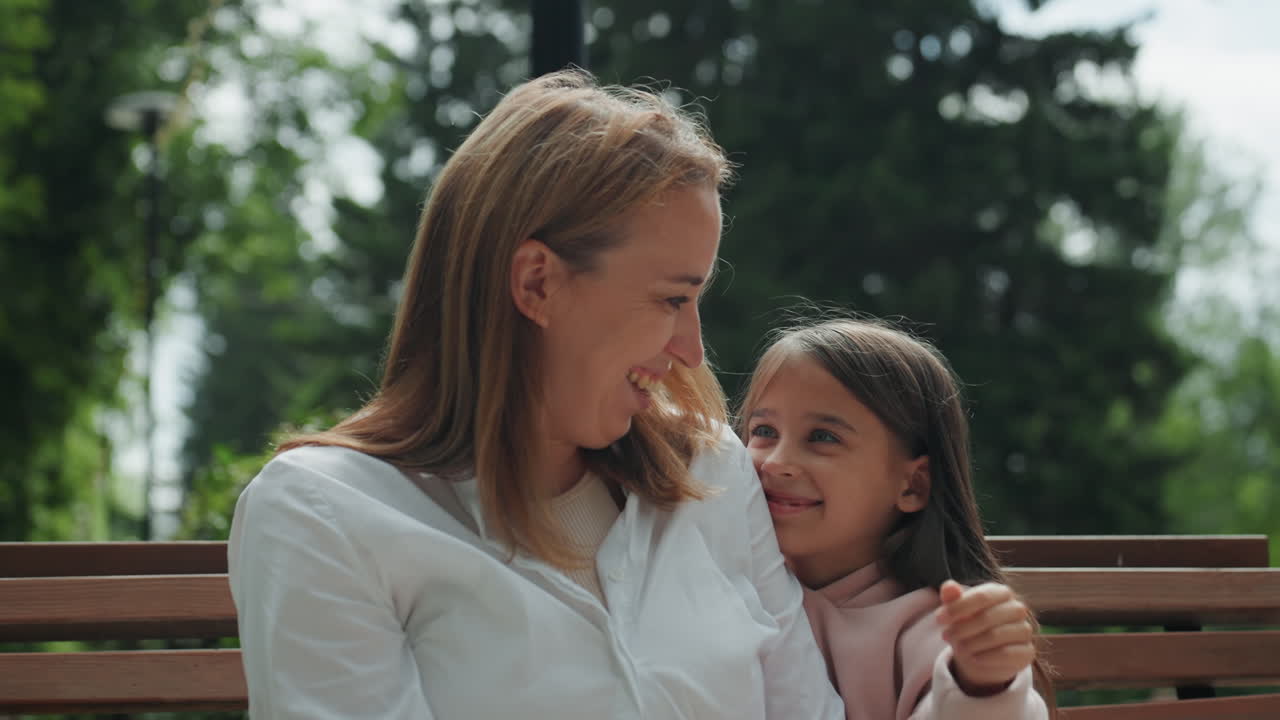 Momento confortante tra madre e figlia. Abbraccio sereno all'aperto tra familiari. Scena rilassata con luce solare calda e un legame delicato. Ambiente sereno di un parco con interazione affettuosa tra madre e figlio.