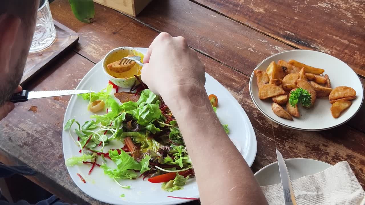 persona comiendo ensalada y papas fritas en un restaurante