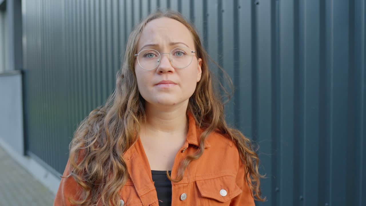 mujer joven nerviosa, preocupada y preocupada mirando a su alrededor en el frío al aire libre con una chaqueta naranja