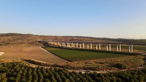 vista aérea de un largo puente de carretera sobre un paisaje con campos y prados al atardecer en israel