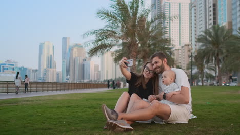 Familia-Feliz-Con-Dos-Niños-Sentados-Juntos-En-El-Césped-Del-Parque-Y-Tomándose-Un-Selfie.-Con-Teléfono-Inteligente.