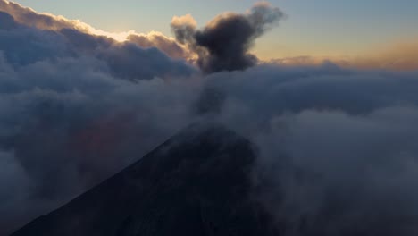Volcan de Fuego at dusk, aerial view of volcano in clouds emitting ash plume, aerial drone establishing shot