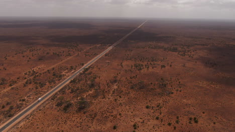 Toma-Cinematográfica-De-Una-Furgoneta-Blanca-De-Gira-Conduciendo-Por-Una-Carretera-Vacía-Rodeada-Por-La-Naturaleza-Roja-Y-Estéril-De-Australia---Toma-De-Seguimiento-De-Drones