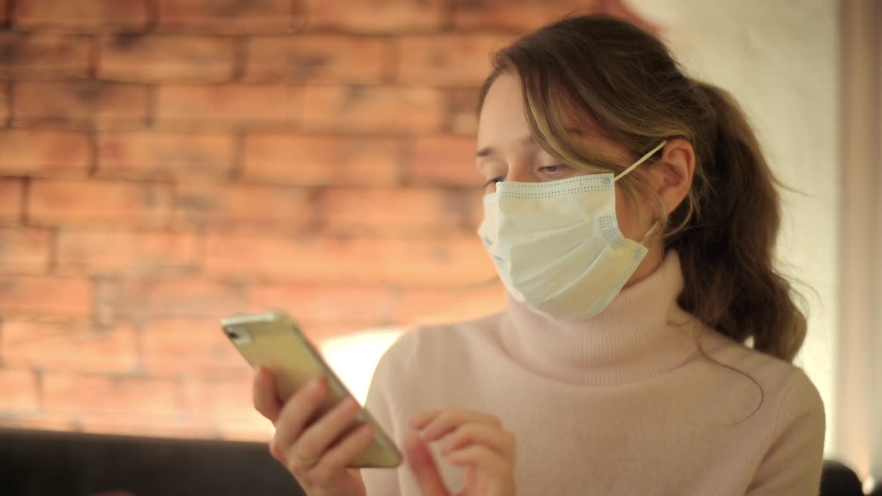 Brunette woman wearing a mask scrolling on her phone at a restaurant