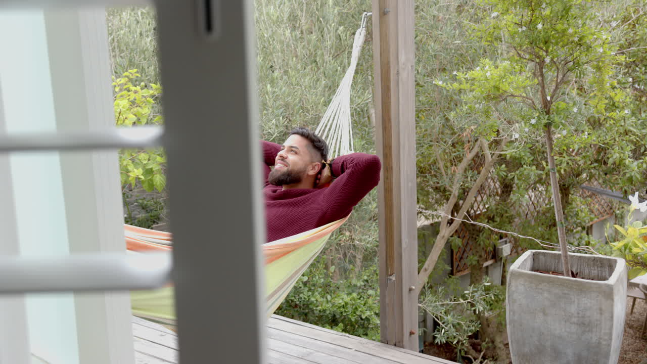 Relaxing in hammock, man enjoying peaceful time outdoors on wooden deck