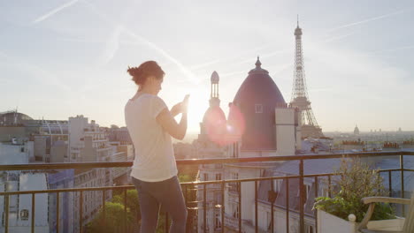 mujer feliz usando un teléfono inteligente enviando mensajes de texto en un balcón en parís francia disfrutando de la vista de la torre eiffel compartiendo experiencias de vacaciones navegando por las redes sociales hermosa puesta de sol