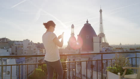 happy woman using smartphone texting on balcony in paris france enjoying view of eiffel tower sharing vacation experience browsing social media beautiful sunset