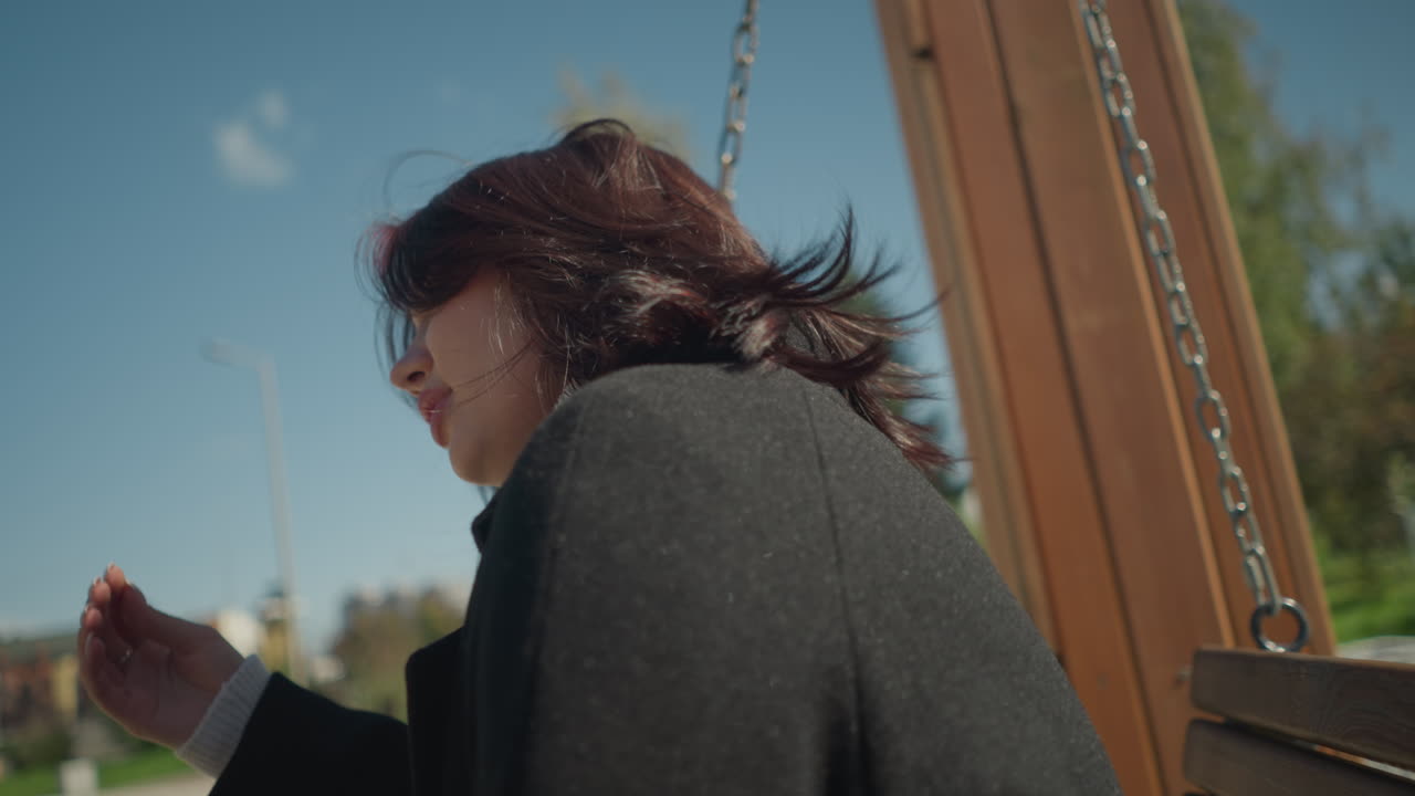 야외에서 흔들리는 동안 미소 짓는 젊은 여자의 클로즈업, 그녀의 머리카락은 바람에 흔들리고, 그녀는 그것을 조정, 밝은 이 공원에서 초록색으로 둘러싸여