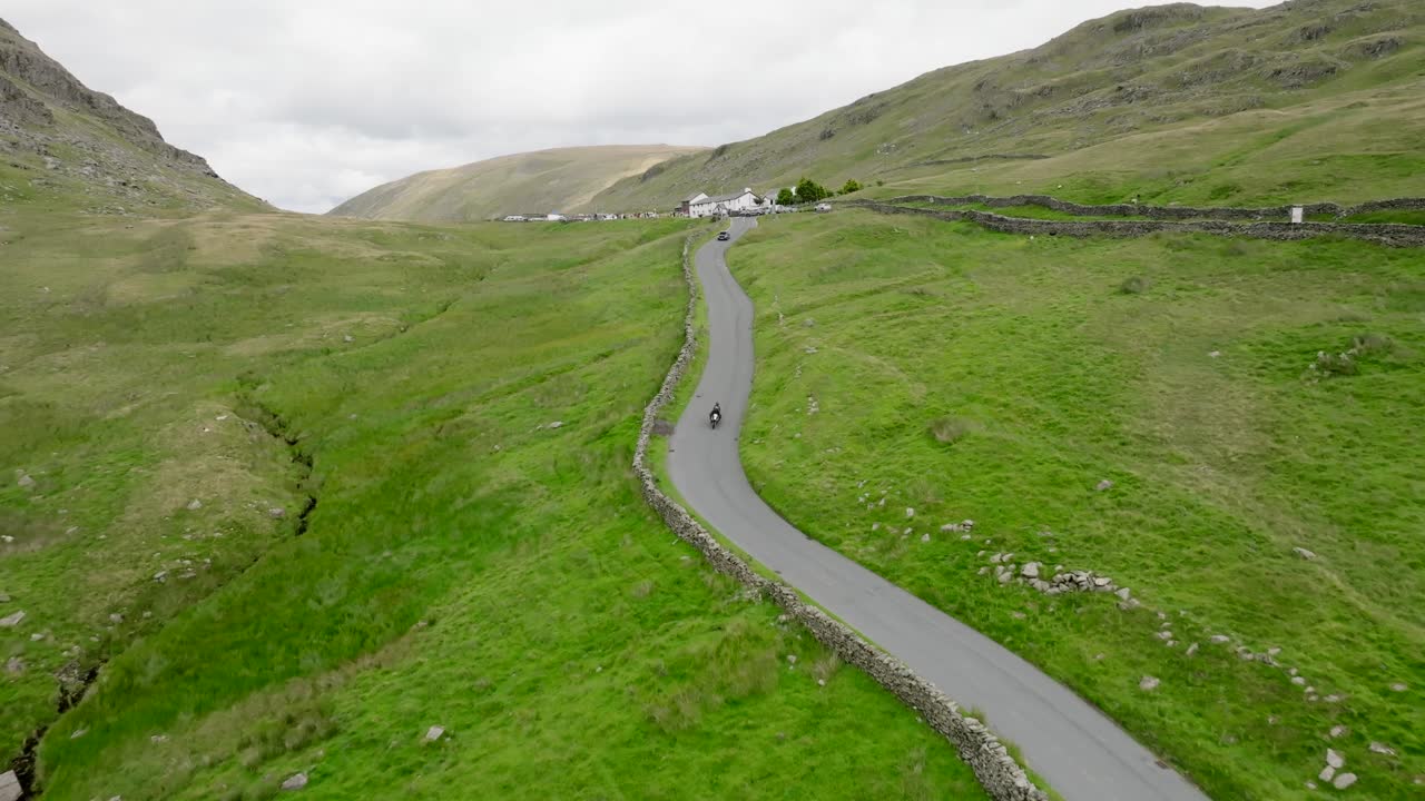 Cars And Motorbike Descending The Struggle From Summit Of The Kirkstone Pass. With View Of The Kirkstone Pass Inn. Summer. Lake District, Cumbria, UK