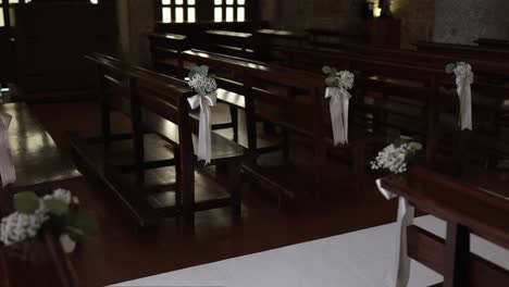 wooden church benches decorated with white flowers and ribbons for wedding ceremony