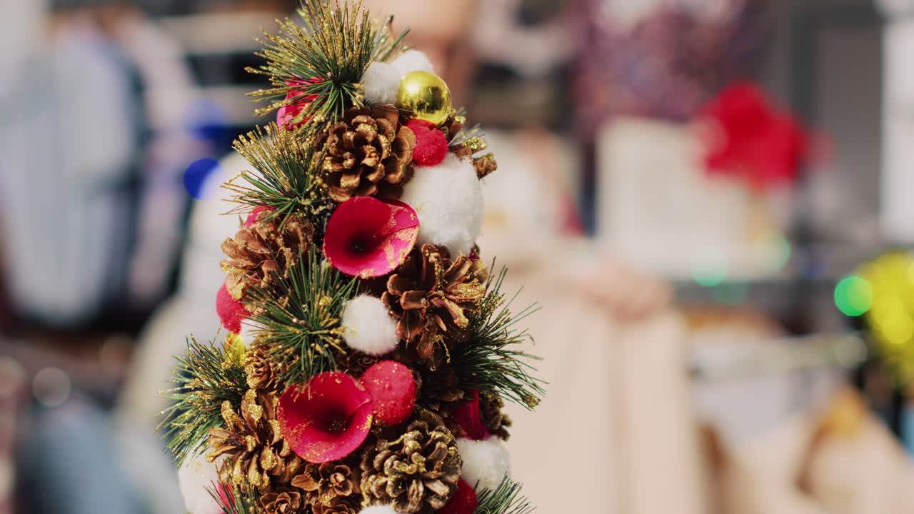 extremo primer plano de un árbol de navidad en miniatura festivo adornado con conos de pino y flores sentado en el mostrador de la tienda de ropa durante la temporada de vacaciones de invierno. decoración de navidad en una boutique de moda