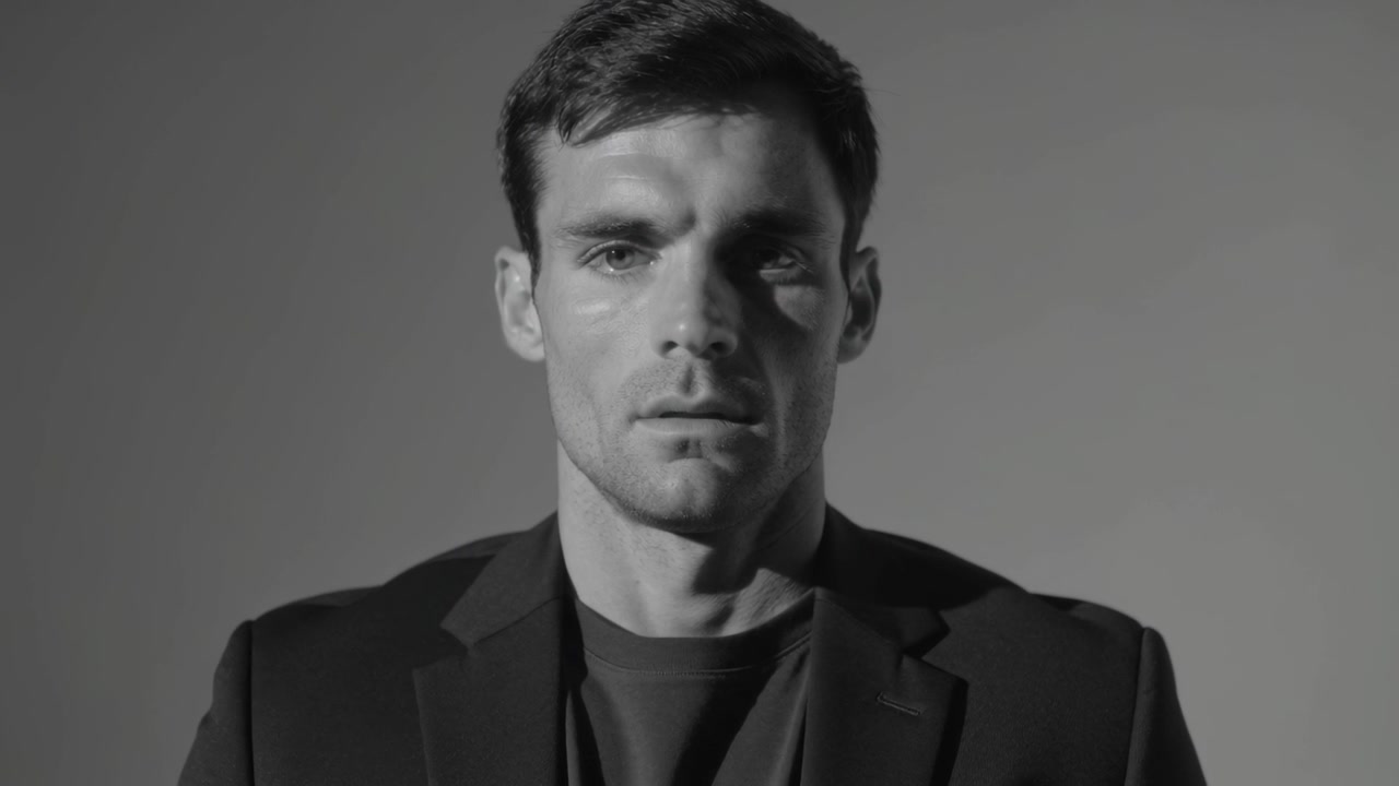 Posing man wearing dark blazer making micro eye shifts, brief blink in studio as light shifts