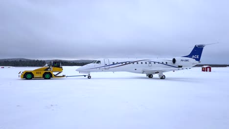 a jet aircraft is being towed across a snowy runway by a yellow pushback vehicle in kiruna, norrbotten county, sweden - medium shot