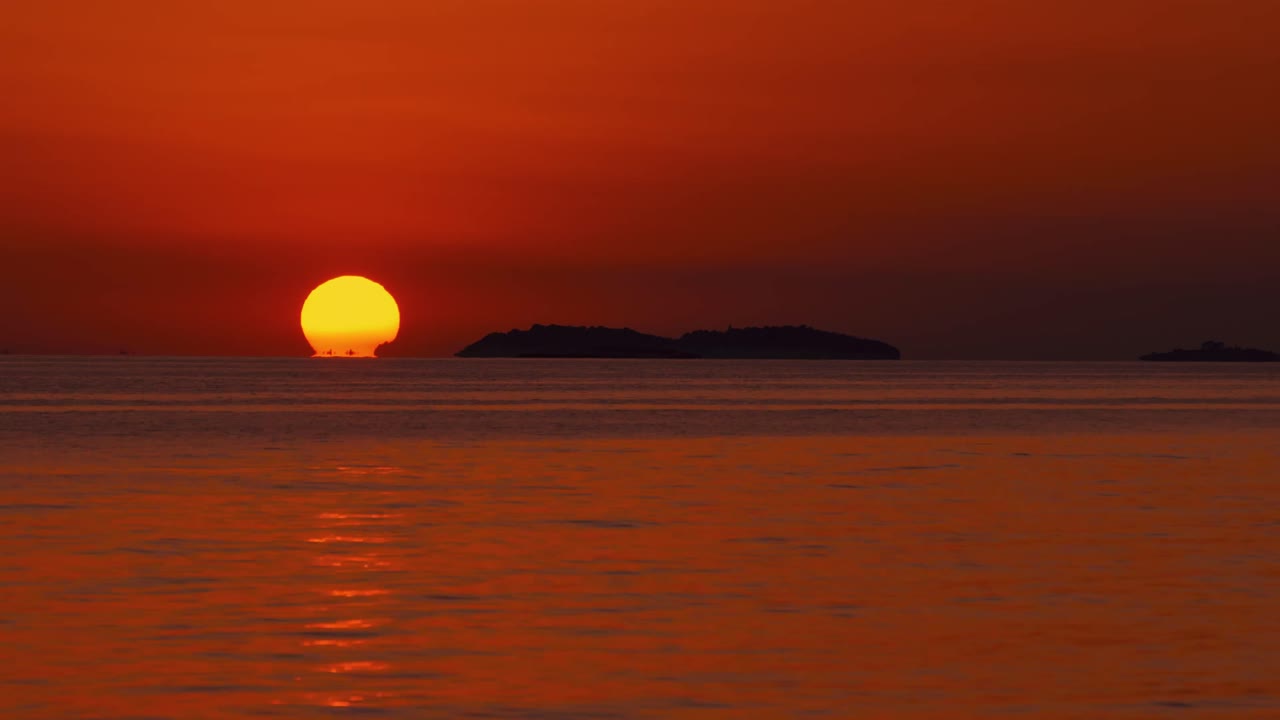크로아티아 지중해 해변의 낭만적인 해변에서 태양이 수평선 너머로 돛배들이 지나가는 커다란 주황색 공으로 지고 있습니다.