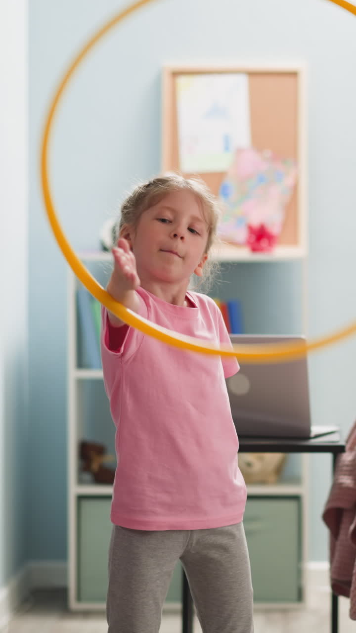 child diligently hula-hooping in bright room where there is notebook, sofa, stillage, children's drawings, doing exercises, close up