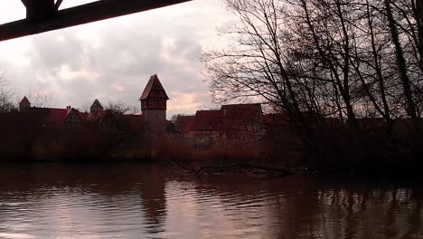 Eine-Drohne-Fliegt-Tief-über-Den-Fluss,-Vorbei-An-Einer-Ente,-Die-Unter-Der-Brücke-Und-über-Den-Wasserfall-An-Einem-Ast-Vorbeigeht