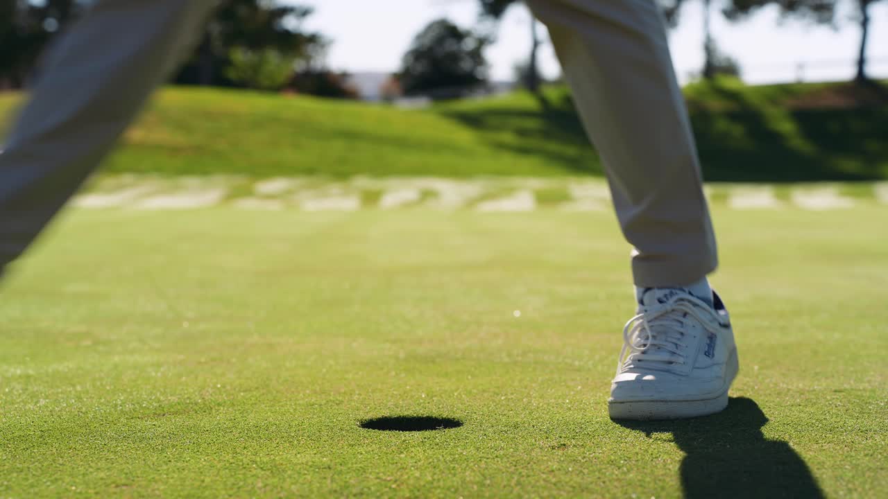 Golfista odpaluje golfový míček do jamky s výrazným stínem táhnoucím se přes green.