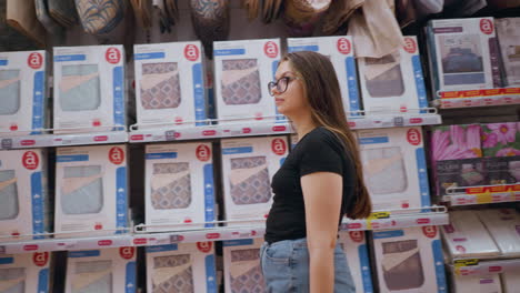 woman shopping in retail store walking past shelf filled with packaged bedding products, she looks around while exploring options, well-lit store aisle filled with home goods and organized displays