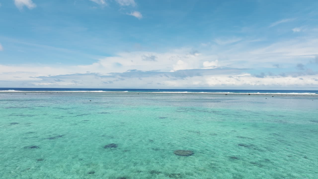 Smooth aerial dolly over glistening green turquoise water of South Pacific, Rarotonga Cook Islands as waves crash into perfect barrels