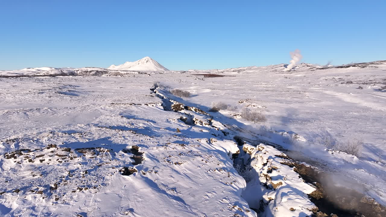 Volcanic steam rising from snow covered crater landscape in Iceland, aerial push forward