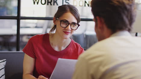 Businesswoman-wearing-glasses-in-talking-with-a-male-colleague-in-a-meeting-room,-over-shoulder-view