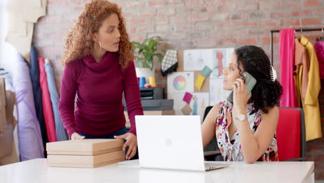 diverse female fashion designers using laptop, on phone and preparing order in studio, slow motion