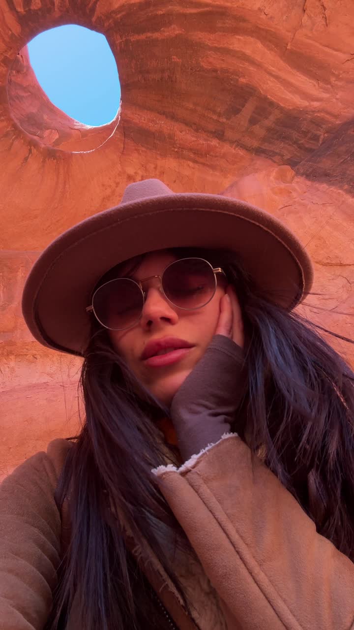 Giovane donna con cappello e occhiali da sole in posa in una grotta di roccia rossa
