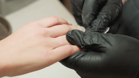 close up view of nail technician wearing black gloves carefully cleaning dust particles from client hand after nail filing session, maintaining cleanliness and precision in manicure process