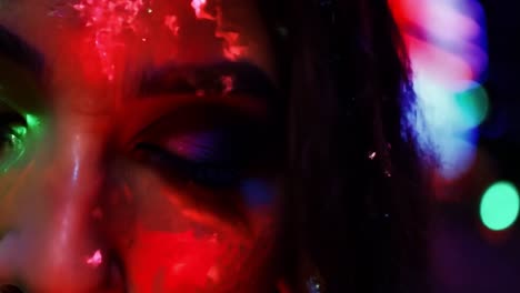 closeup of a model showcasing fluorescent paint on her face while moving her head under ultraviolet light, creating a vibrant and artistic display in a dark nightclub setting