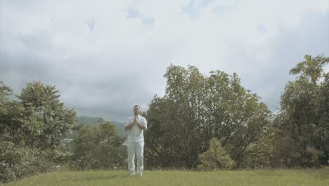 Young man in white Dress doing yoga meditation in a beautiful green landscape in slow motion mindfulness and tai chi