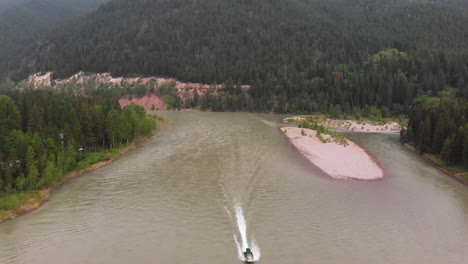 aerial shot of a boat speeding up flathead river, in montana wilderness, drone passes over boat until it's no longer visible