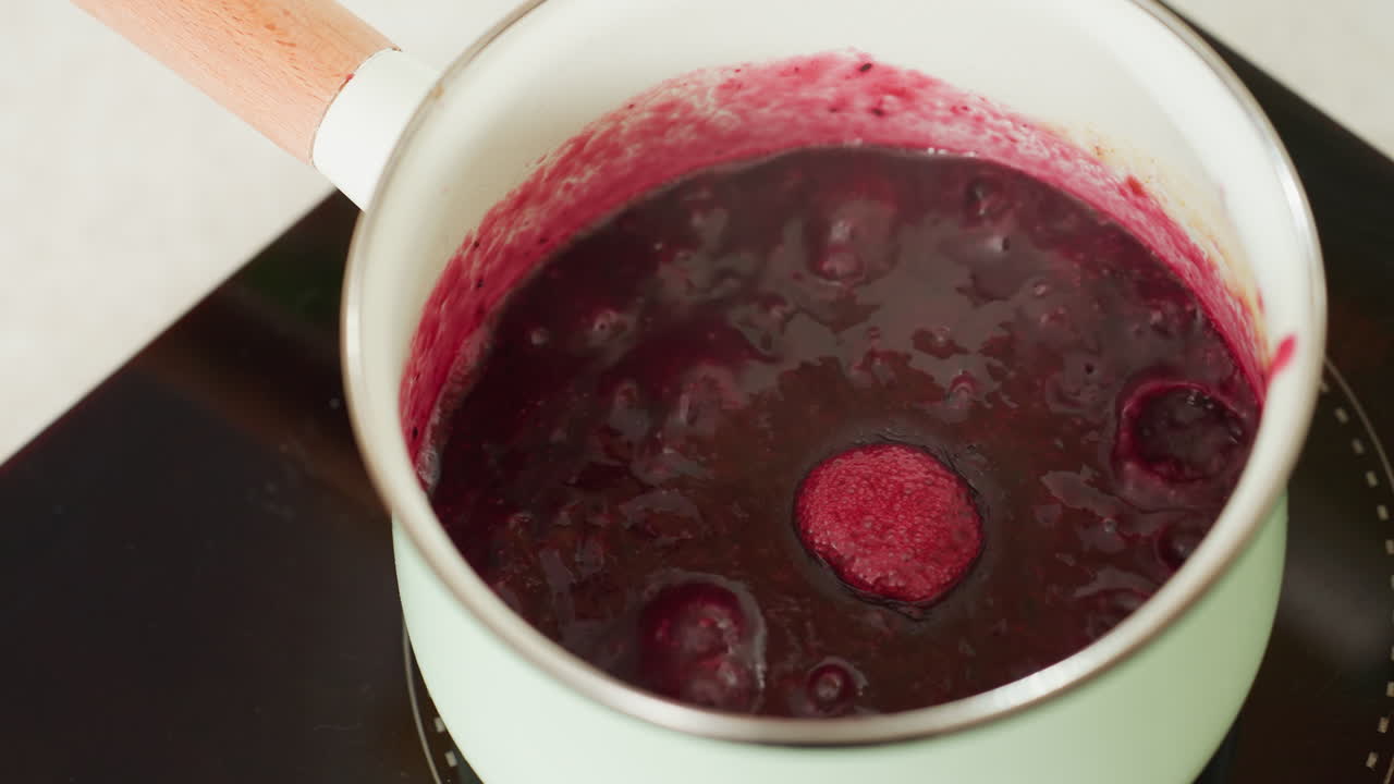 Close up of thick red soup or sauce actively bubbling in pastel green pot on electric stove, capturing texture, heat intensity, and vivid color during cooking process in clean and modern kitchen
