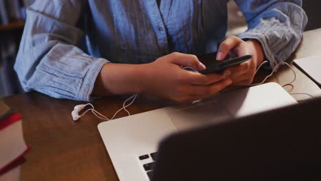 Asian-female-student-sitting-at-a-desk-with-a-laptop-and-using-a-smartphone