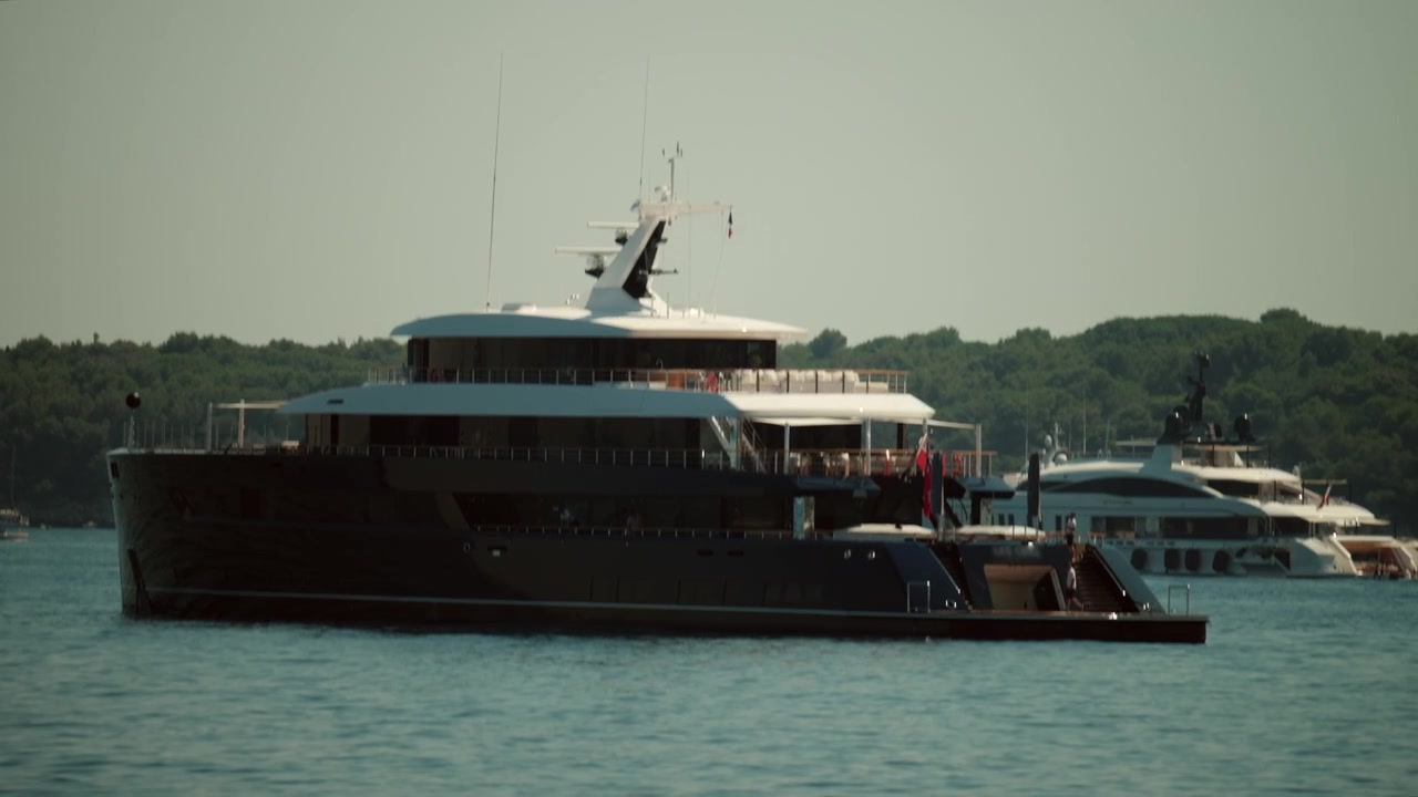 Superyacht blu scuro "Les Cinq" che naviga in acque calme, mostrando viaggi opulenti, vacanze al mare e uno stile di vita di lusso, Golfe Juan, Francia.