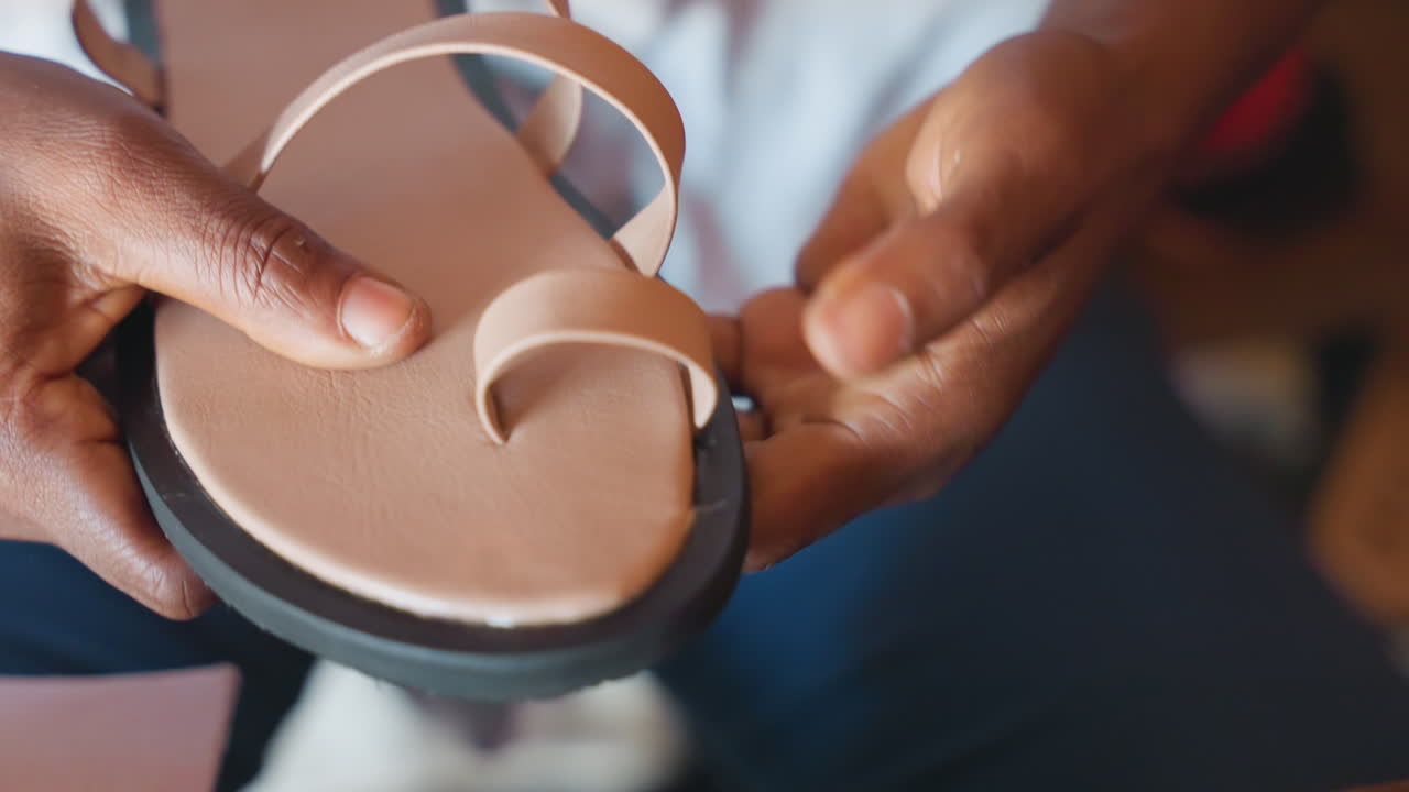 Pengrajin menyelesaikan tali sandal kulit dengan penghalusan dan pemolesan yang cermat, tangan close-up memeriksa kesesuaian, penghalusan tepi, inspeksi taktil, dan presentasi produk akhir di lingkungan studio yang intim.