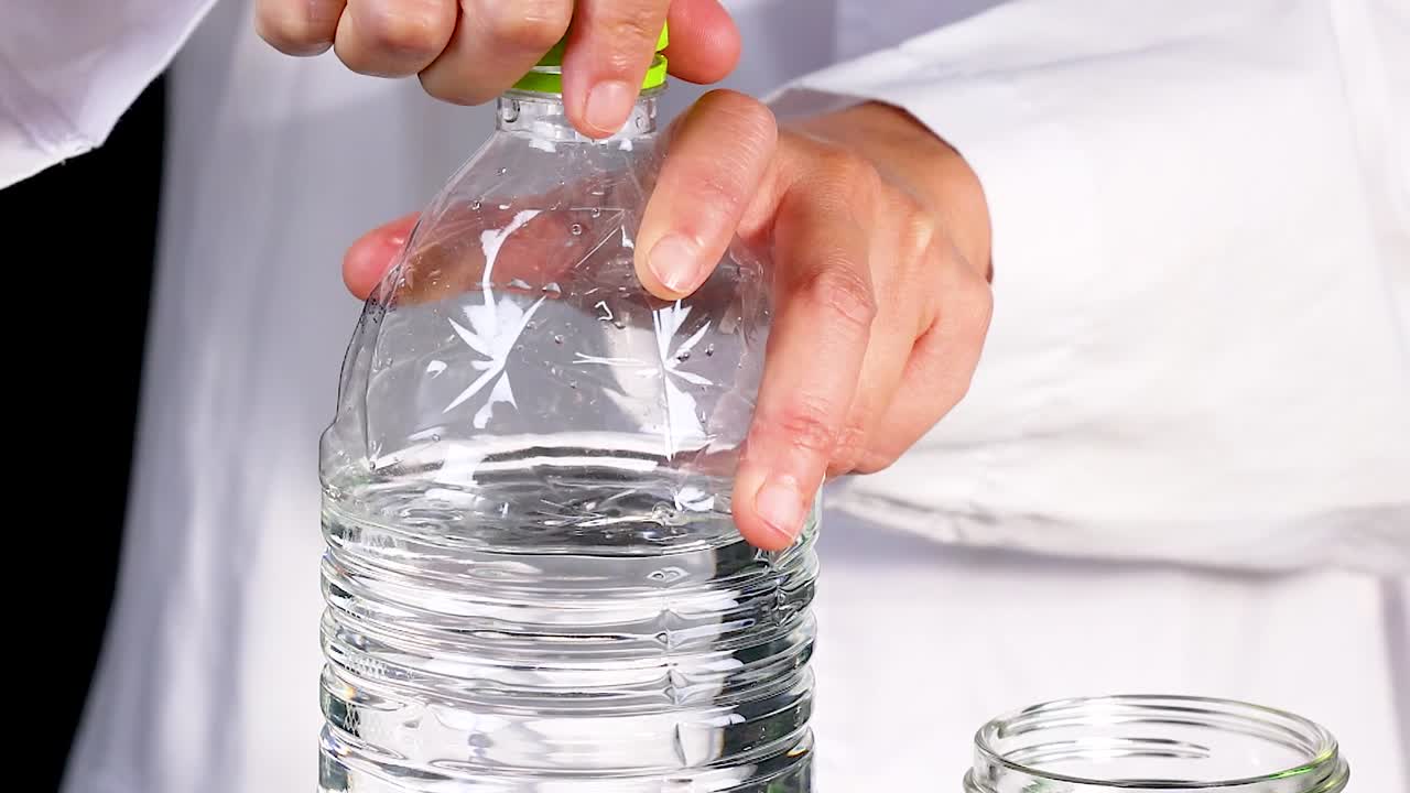 Close-up of hands in a lab coat opening a water bottle against a black background.