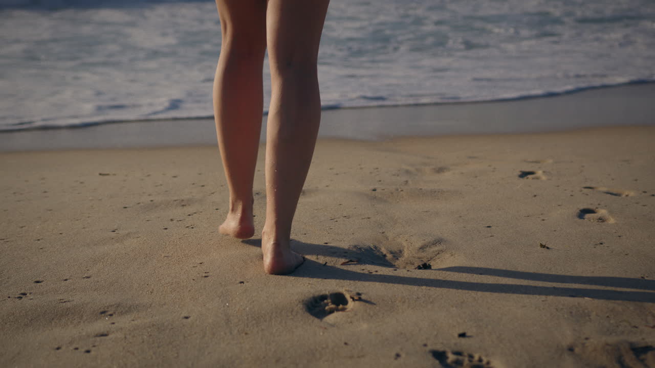 una ragazza che cammina verso il mare con un'onda in arrivo in slow motion