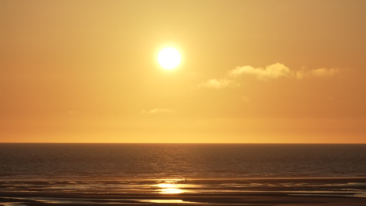 Fredfyldt solnedgang eller solopgang over et roligt hav ved en sandstrand med klar horisont