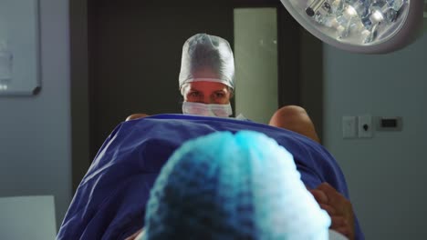 vista frontal de una cirujana caucásica examinando a una mujer embarazada durante el parto en la sala de operaciones en